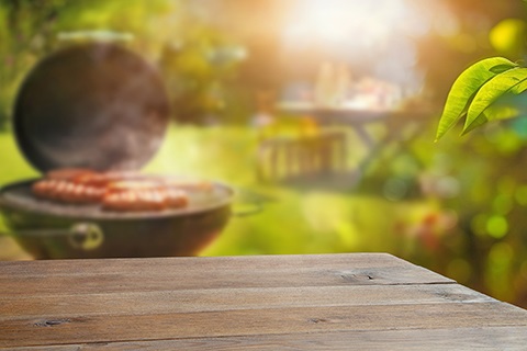 A backyard barbecue. An empty table with hot dogs grilling in the background.