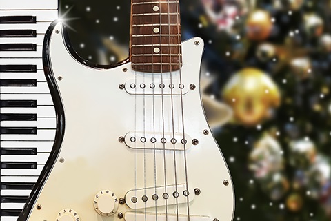 A guitar up against a keyboard with holiday lighting in the background.